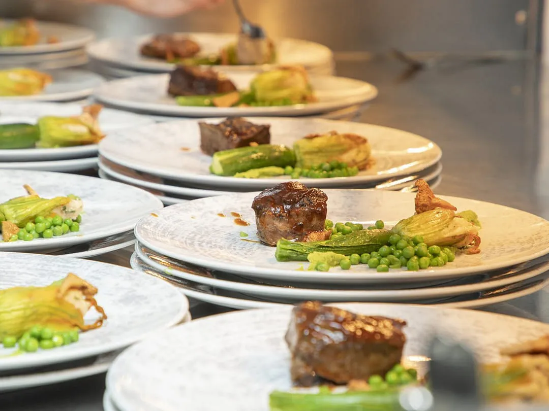 Angerichtete Teller mit Fleisch, Zucchiniblüte und Erbsen in der Küche